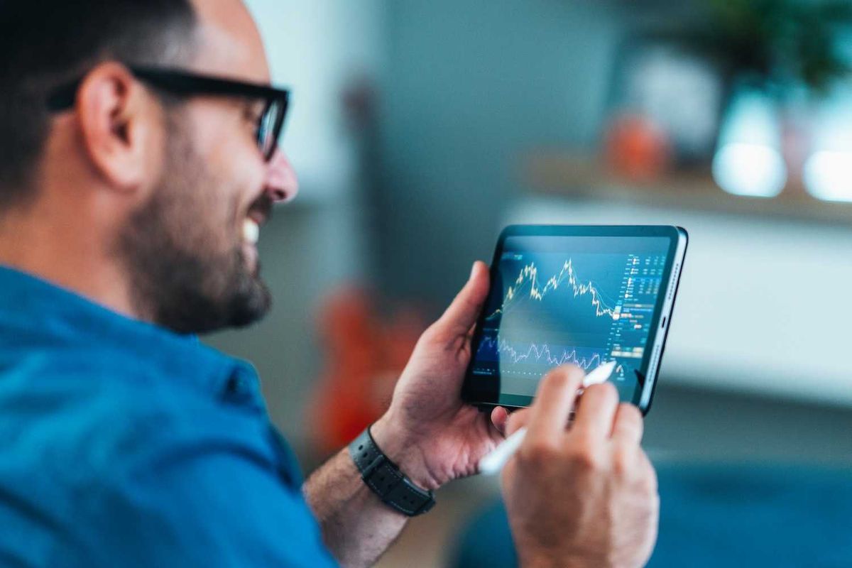 Smiling man analyzing stock market charts on a tablet with a stylus.