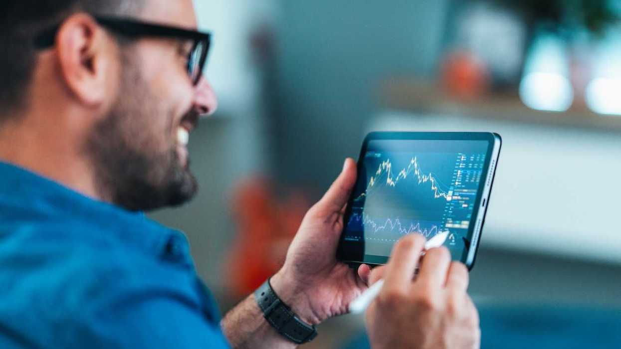 Smiling man analyzing stock market charts on a tablet with a stylus.