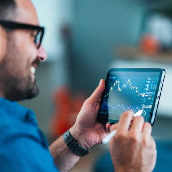 Smiling man analyzing stock market charts on a tablet with a stylus.