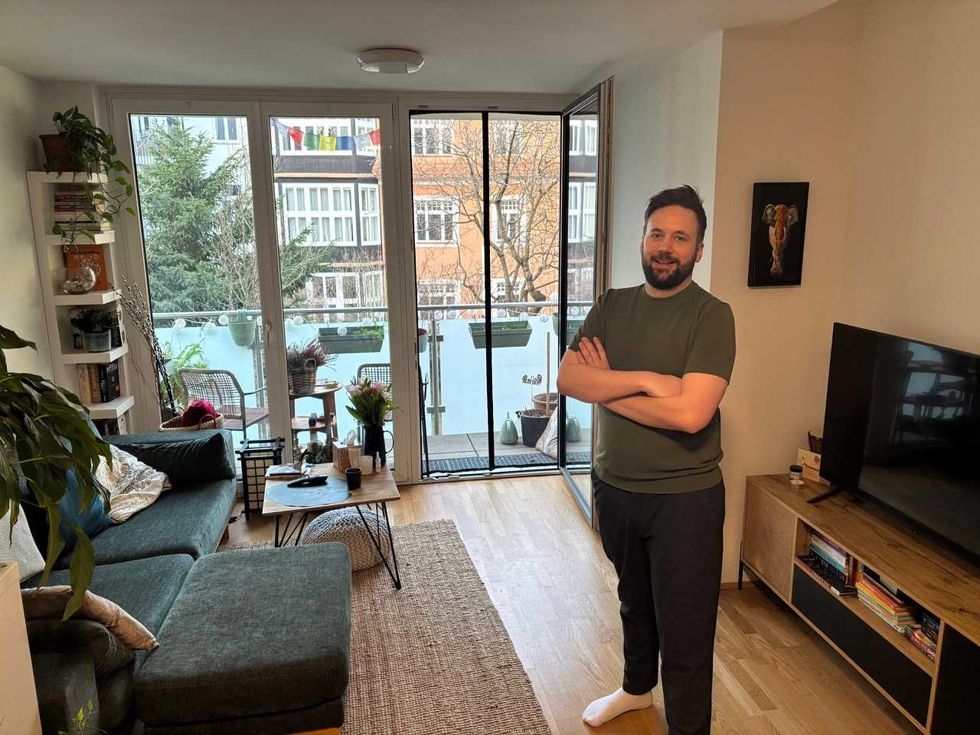 Smiling man in a bright, modern living room with a balcony view of Vienna