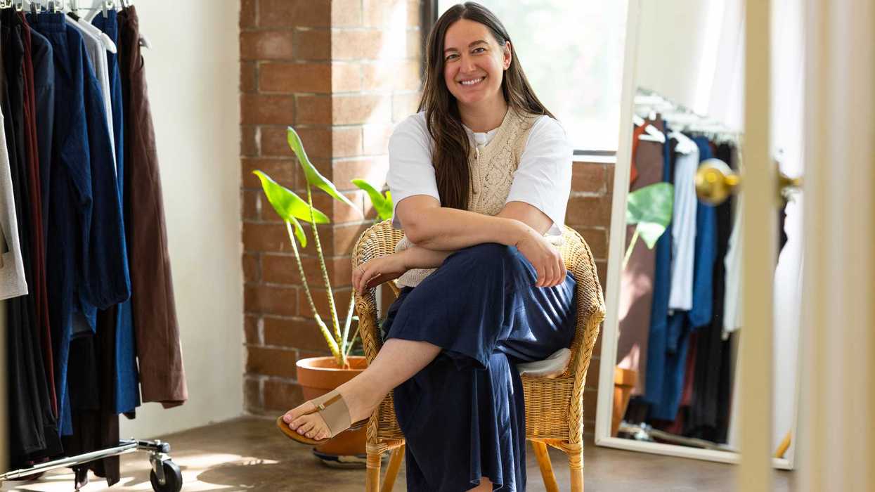 Smiling woman in white shirt and vest sits in a wicker chair in a clothing store