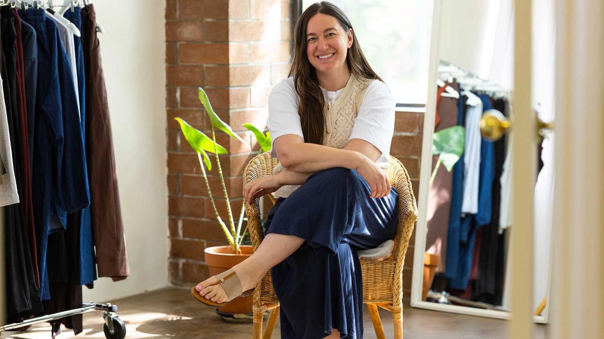 Smiling woman in white shirt and vest sits in a wicker chair in a clothing store