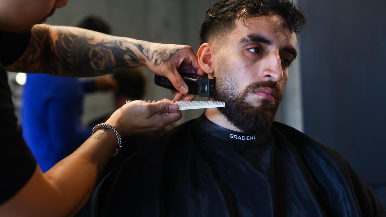 Tattooed barber trimming a man's beard with an electric trimmer and comb
