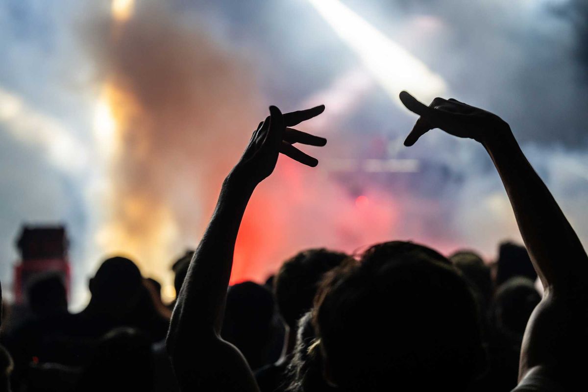 The view of a smoky concert from the crowd with people making hand signs in the air