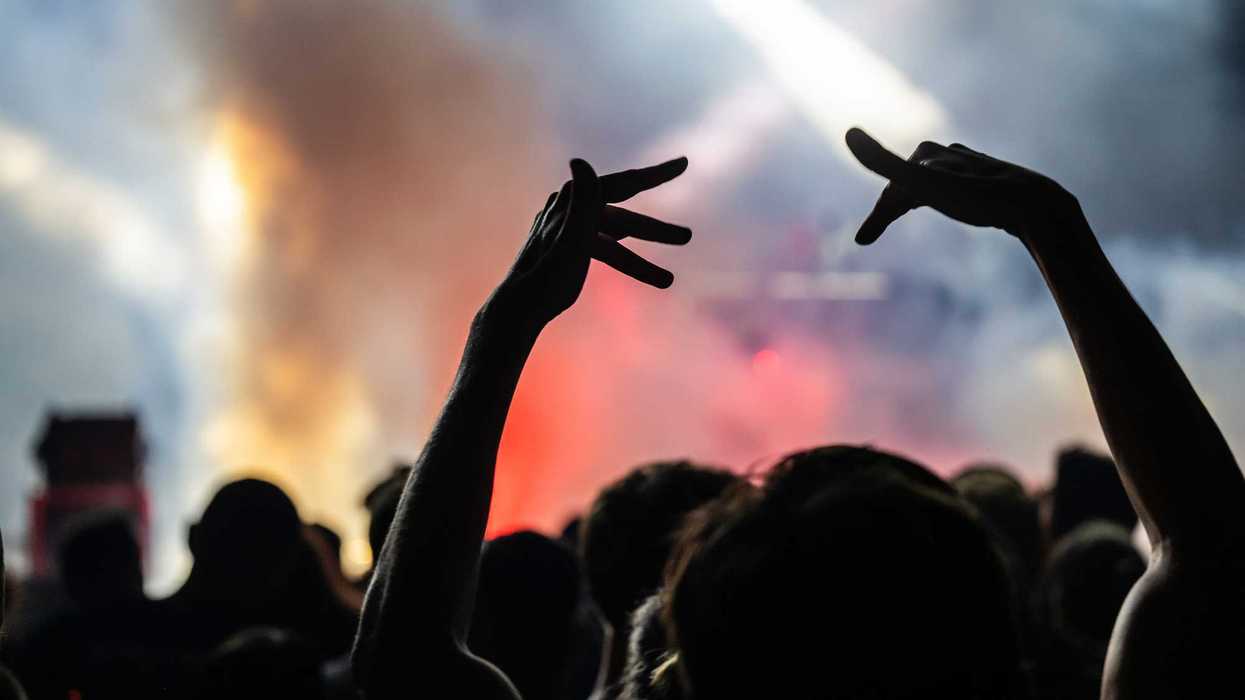 The view of a smoky concert from the crowd with people making hand signs in the air