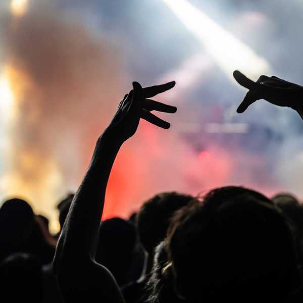 The view of a smoky concert from the crowd with people making hand signs in the air
