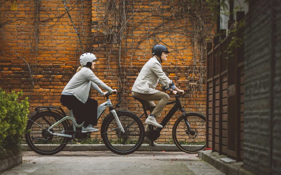Two urban cyclists ride e-bikes through the city