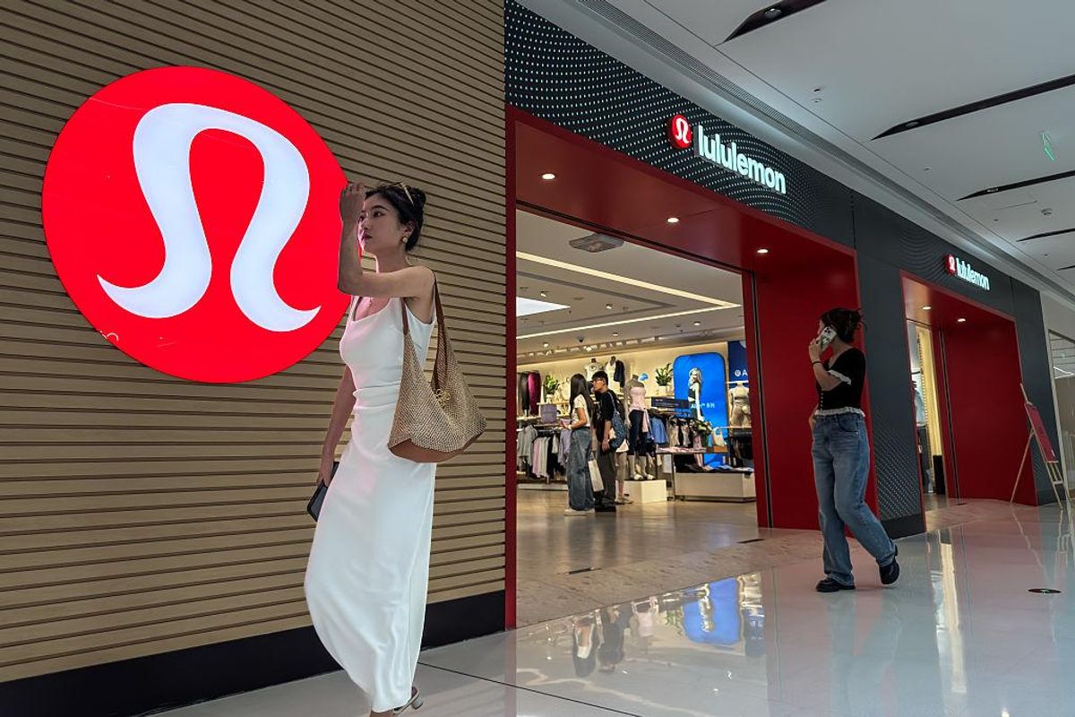 Two women at a Lululemon store, one walking past the logo, another near the entrance.