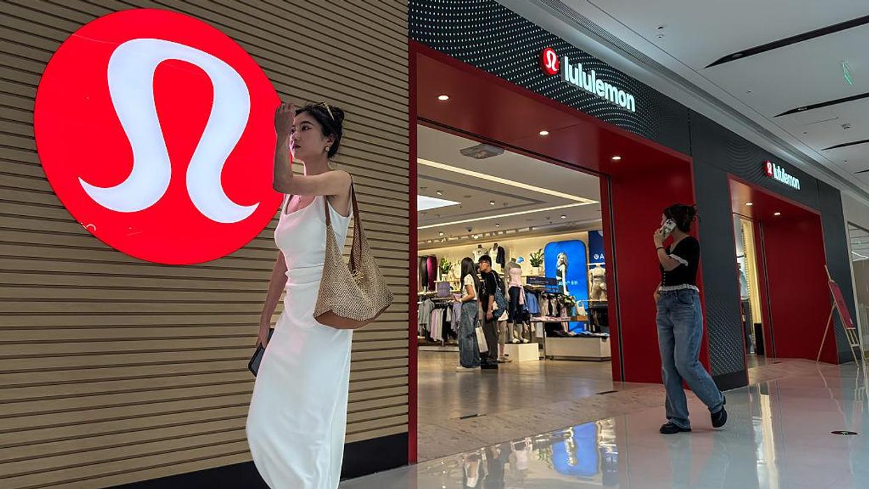 Two women at a Lululemon store, one walking past the logo, another near the entrance.