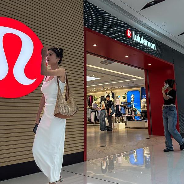 Two women at a Lululemon store, one walking past the logo, another near the entrance.