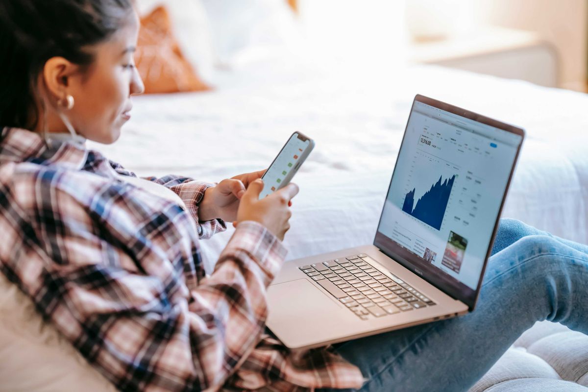Woman analyzing financial charts on laptop and phone
