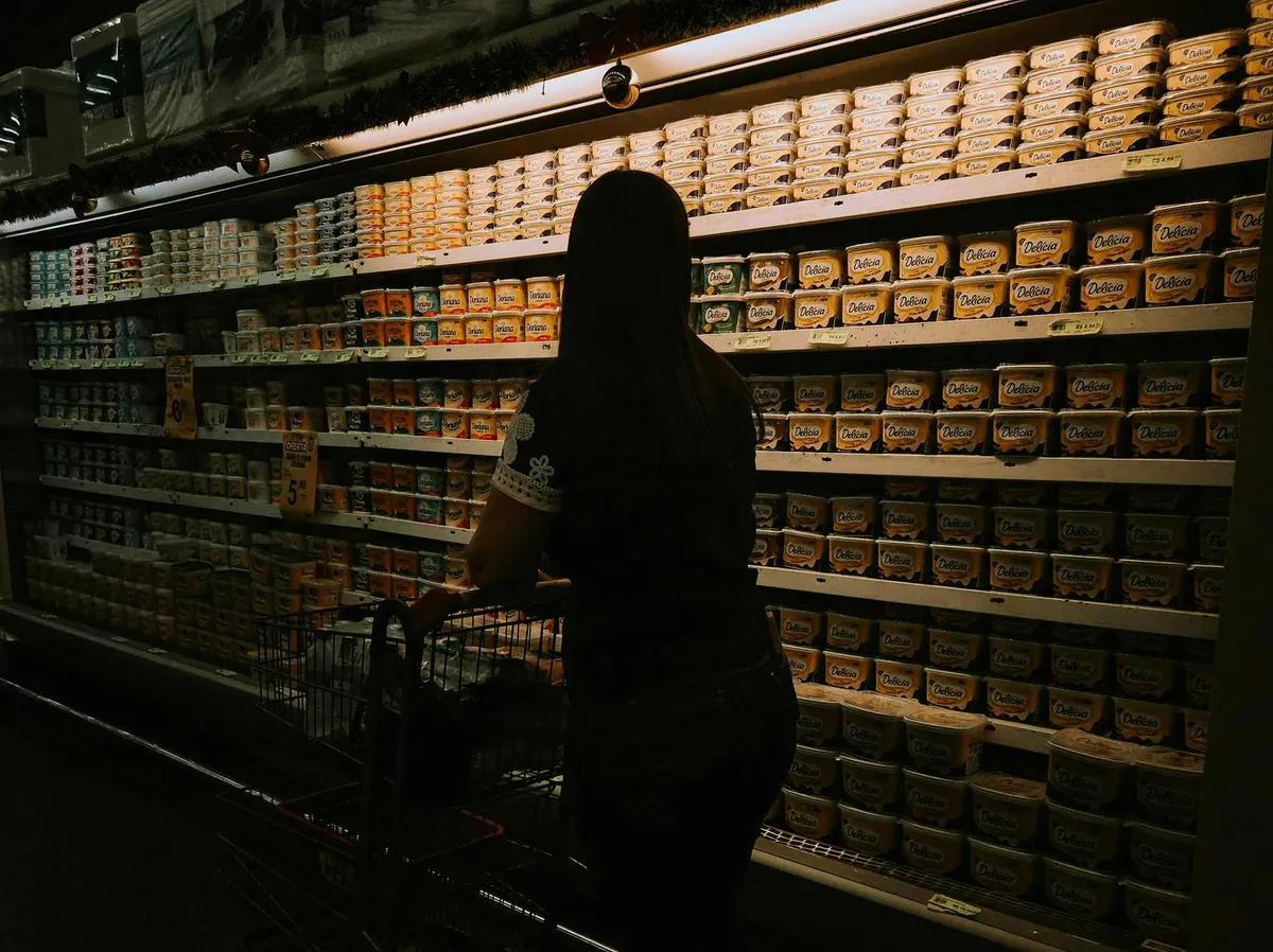 Woman with shopping cart facing a grocery store refrigerator aisle