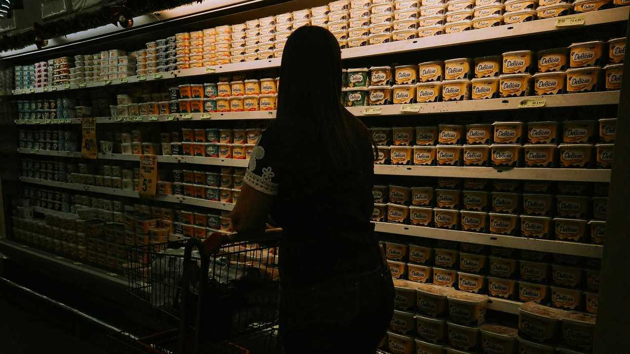Woman with shopping cart facing a grocery store refrigerator aisle