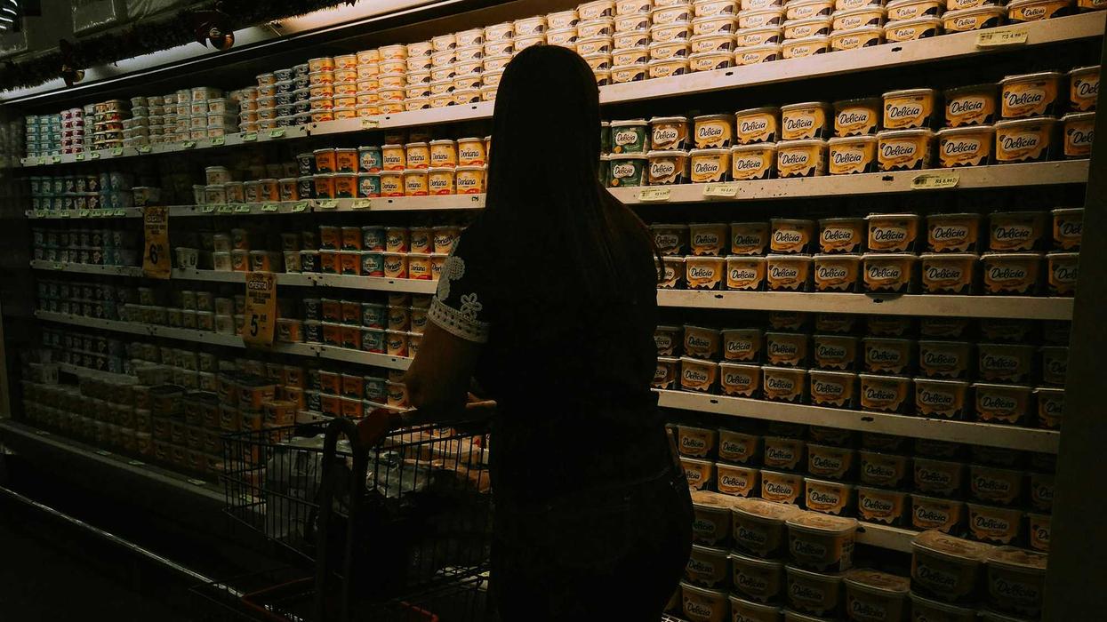 Woman with shopping cart facing a grocery store refrigerator aisle