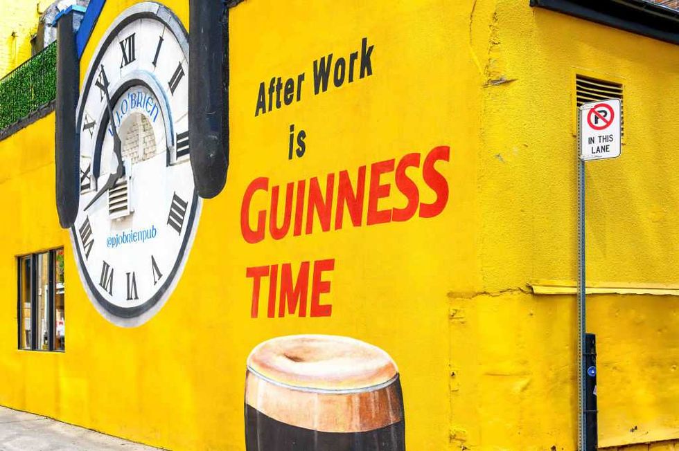 Yellow building wall mural with a clock, 'After Work is GUINNESS TIME' text, and a Guinness pint.