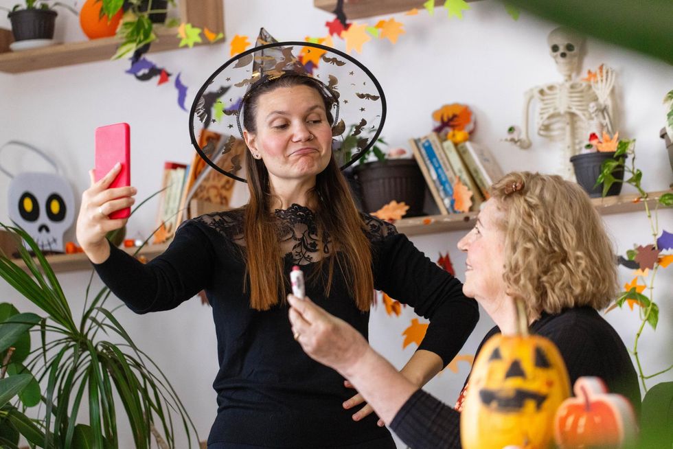 Young woman in witch hat makes funny face for selfie with older woman during Halloween.